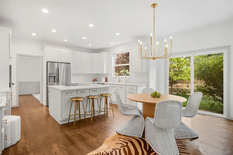 Remodeled white kitchen with island seating, brass chandelier and sliding glass doors to the yard at 869 Shadowstone Dr in Weatherstone, Highlands Ranch
